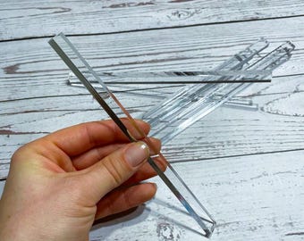 May include: Clear acrylic rectangular strips, some held in a hand, others scattered on a light wood surface. The strips are reflective, with a mirrored appearance. The edges are clean and sharp, suggesting a modern design.