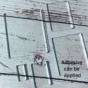 May include: Several clear, rectangular acrylic pieces are displayed on a light wooden surface. The text "Adhesive can be applied" is next to one of the pieces, suggesting their use. The pieces are transparent and have rounded corners.