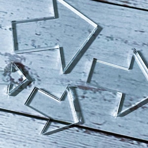 Puede incluir: Colección de piezas de acrílico transparente en forma de flecha. Las flechas varían en tamaño y están dispuestas sobre una superficie azul claro con vetas de madera. El material transparente permite el paso de la luz, creando sombras.