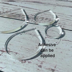 Pode incluir: Formas de lágrima de acrílico transparente em vários tamanhos. As formas são transparentes e têm um acabamento liso e polido. O texto "Adhesive can be applied" é visível. Adequado para artesanato e projetos DIY.