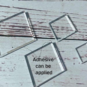 Può includere: Diverse forme quadrate trasparenti in acrilico di varie dimensioni sono disposte su una superficie chiara con venature del legno. Il testo "Adhesive can be applied" è visibile su uno dei pezzi. I pezzi sono trasparenti.