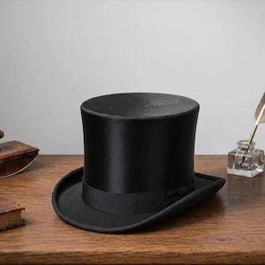 Könnte beinhalten: Ein klassischer schwarzer Zylinderhut mit breiter Krempe und Satinband. Der Hut besteht aus einem glatten, glänzenden Material und liegt auf einer Holzoberfläche. Ein traditionelles formelles Accessoire.