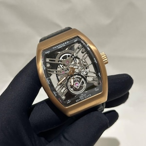 Puede incluir: Un reloj Franck Muller Vanguard dorado con una correa de cuero negro. La esfera del reloj es esqueleto, revelando los intrincados mecanismos internos. El reloj tiene el texto "VANGUARD NORTH" y "SOUTH SEVEN DAYS" en la esfera.