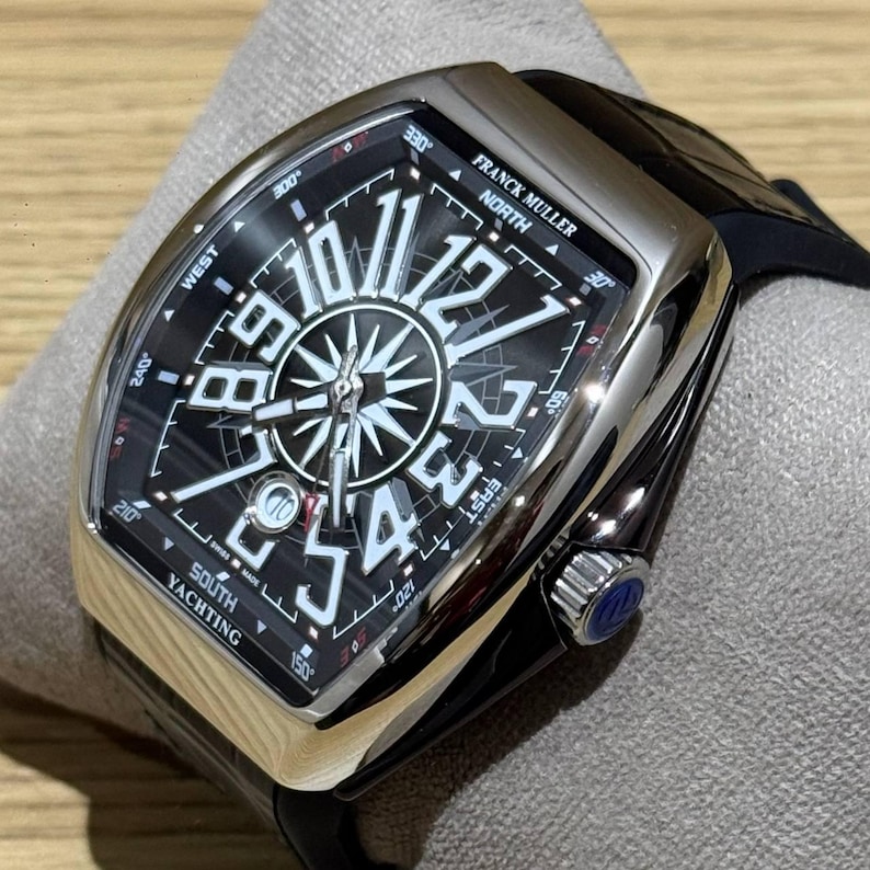 May include: A luxury wristwatch with a black face and silver casing. The watch features a compass rose design with large white numerals and the text "FRANCK MULLER NORTH SOUTH YACHTING". The watch has a black leather strap.
