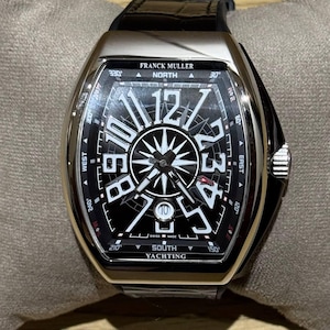 May include: A luxury Franck Muller watch with a black face and silver casing. The watch features large white numerals, a compass design, and the text "SOUTH YACHTING". The watch has a black leather band.