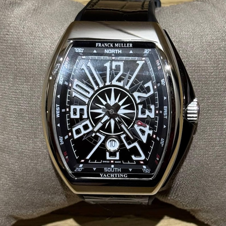 May include: A luxury Franck Muller watch with a black face and silver casing. The watch features large white numerals, a compass design, and the text "SOUTH YACHTING". The watch has a black leather band.