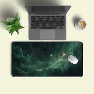 May include: A rectangular mouse mat with a green nebula design, a white mouse, and a laptop. The mouse mat features a crescent moon and stars. A small potted plant and a cup of coffee are also visible.