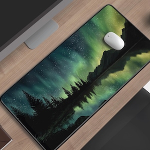 Könnte beinhalten: Rechteckige Schreibtischunterlage mit einem Landschaftsdesign, das grüne und blaue Nordlichter über einem Wald und Bergen zeigt. Eine weiße Computermaus liegt auf der Matte. Eine Tasse Kaffee und ein kleines Notizbuch sind ebenfalls zu sehen.