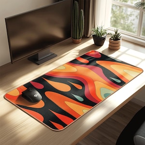 Puede incluir: Alfombrilla de ratón rectangular con un diseño abstracto y colorido. El patrón presenta formas fluidas en tonos naranja, rojo, amarillo y verde azulado sobre un fondo negro. Un ratón de ordenador negro está en el lado izquierdo de la alfombrilla. La alfombrilla está sobre un escritorio de madera.