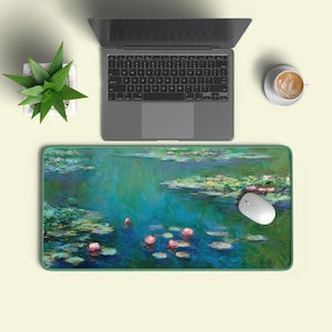 Könnte beinhalten: Eine rechteckige Schreibtischunterlage mit einem impressionistischen Gemälde von Seerosen in einem Teich, in Grün-, Blau- und Rosatönen. Eine weiße Maus liegt auf der Unterlage, neben einem Laptop und einer Tasse Kaffee.