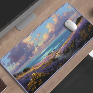 Puede incluir: Alfombrilla de ratón rectangular con un diseño de paisaje costero. La imagen muestra un cielo vibrante, un mar azul y campos de flores moradas y amarillas. Un ratón de ordenador blanco descansa sobre ella. Mide unos 70 cm de largo.