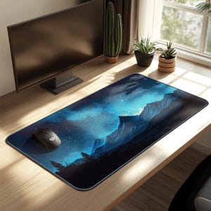 Puede incluir: Alfombrilla de ratón rectangular con un paisaje montañoso nocturno y un cielo estrellado en tonos azules y negros. Un ratón de ordenador negro está sobre la alfombrilla. La alfombrilla está sobre un escritorio de madera.