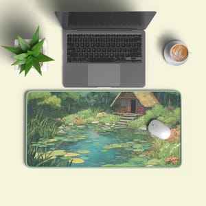 May include: A rectangular mouse mat with a tranquil scene of a pond, a small cabin, and verdant foliage. A laptop, a white mouse, a cup of coffee, and a potted plant are also visible on a pale yellow surface.