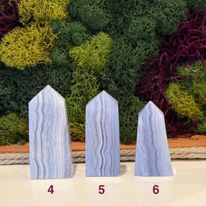 May include: Three blue lace agate obelisks with white veining, numbered 4, 5, and 6. The obelisks are displayed against a backdrop of green, yellow, and burgundy moss.