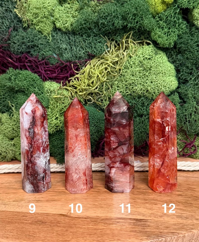 May include: Four red quartz crystal points with varying shades of red and white. Each crystal is numbered at the base. The background features green and purple moss.
