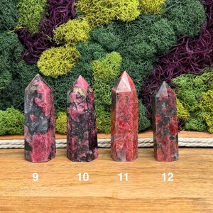 Puede incluir: Cuatro torres de piedras preciosas pulidas en tonos de rojo, rosa y negro, cada una con una parte superior puntiaguda. Las piedras est&aacute;n numeradas 9, 10, 11 y 12. El fondo presenta una mezcla de musgo verde, amarillo y morado.