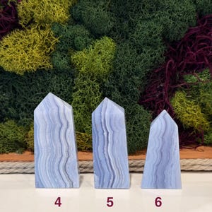 May include: Three blue lace agate obelisks with white and gray banding. The obelisks are numbered 4, 5, and 6 at the base. The background features a variety of green, yellow, and purple moss.