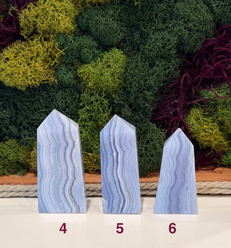 May include: Three blue lace agate obelisks with white and gray banding. The obelisks are numbered 4, 5, and 6 at the base. The background features a variety of green, yellow, and purple moss.