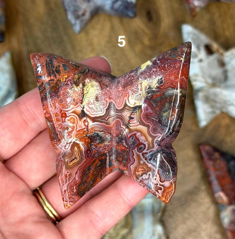 May include: A butterfly-shaped stone carving with intricate patterns in shades of red, brown, and cream. The stone has a polished, glossy finish. The number "5" is visible on the top of the carving. Other stone carvings are visible in the background.