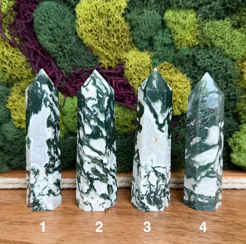 May include: Four polished tree agate crystal towers, each with a unique pattern of white and green swirls. The crystals are numbered 1 through 4, and stand upright against a backdrop of green and brown moss.