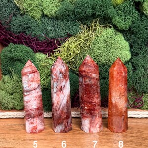 May include: Four red quartz crystal towers with varying patterns and shades of red and white. The crystals are numbered 5, 6, 7, and 8. The background features green and burgundy moss.