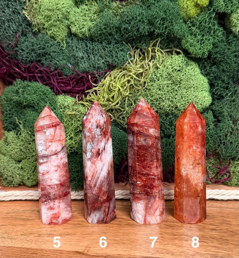 May include: Four red quartz crystal towers with varying patterns and shades of red and white. The crystals are numbered 5, 6, 7, and 8. The background features green and burgundy moss.