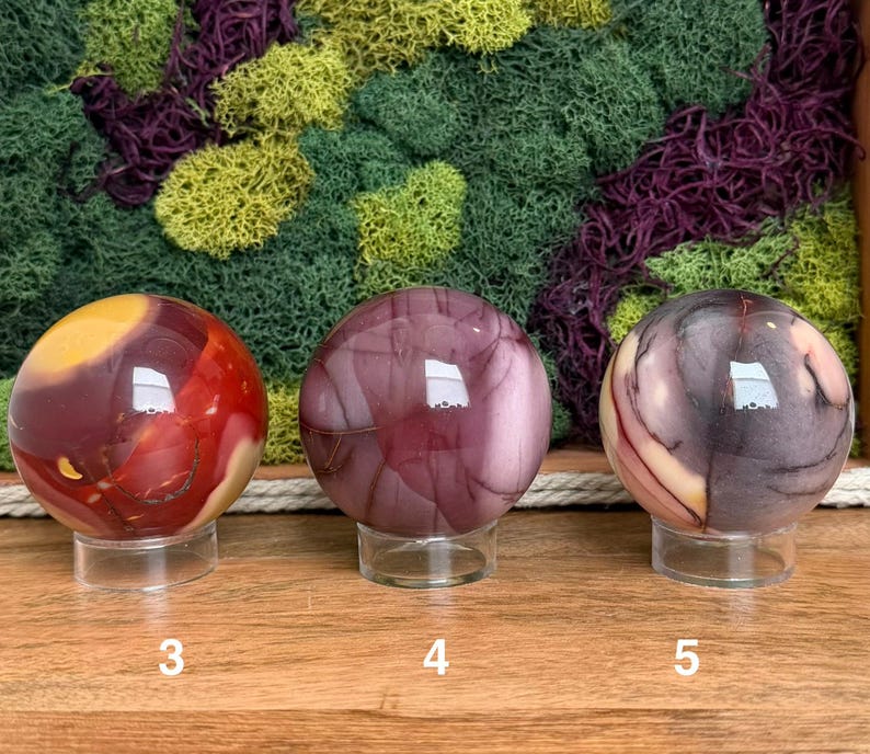 Puede incluir: Tres piedras esf&eacute;ricas pulidas sobre soportes circulares transparentes. La primera esfera es roja y amarilla, la segunda es de color malva s&oacute;lido con vetas oscuras y la tercera es una mezcla de morado oscuro, crema y rojo. Etiquetadas 3, 4 y 5.