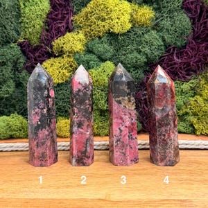 Puede incluir: Cuatro torres de cristal pulido con una mezcla de tonos negros y rosas. Cada torre tiene una parte superior puntiaguda y una base rectangular. Los cristales est&aacute;n numerados del 1 al 4. El fondo presenta una variedad de musgos verdes, amarillos y morados.