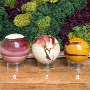 Puede incluir: Tres esferas de piedra pulida sobre soportes circulares transparentes. La esfera 6 es de color malva oscuro con la parte superior blanca. La 7 es crema con vetas rojo oscuro. La 8 es amarillo mostaza con vetas rojo oscuro. N&uacute;meros 6, 7 y 8.