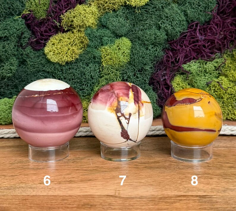 Puede incluir: Tres esferas de piedra pulida sobre soportes circulares transparentes. La esfera 6 es de color malva oscuro con la parte superior blanca. La 7 es crema con vetas rojo oscuro. La 8 es amarillo mostaza con vetas rojo oscuro. N&uacute;meros 6, 7 y 8.