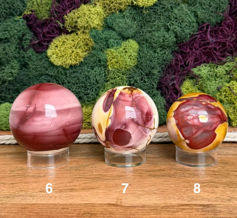 Puede incluir: Tres piedras esf&eacute;ricas pulidas sobre soportes circulares transparentes. La primera esfera es de color granate oscuro con bandas sutiles. La segunda es una mezcla de crema, amarillo y granate. La tercera es amarilla con grandes manchas granates.