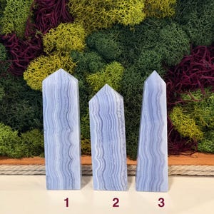 May include: Three blue lace agate obelisks with a layered, banded pattern. The obelisks are numbered 1, 2, and 3. The background features a variety of green, yellow, and red moss.