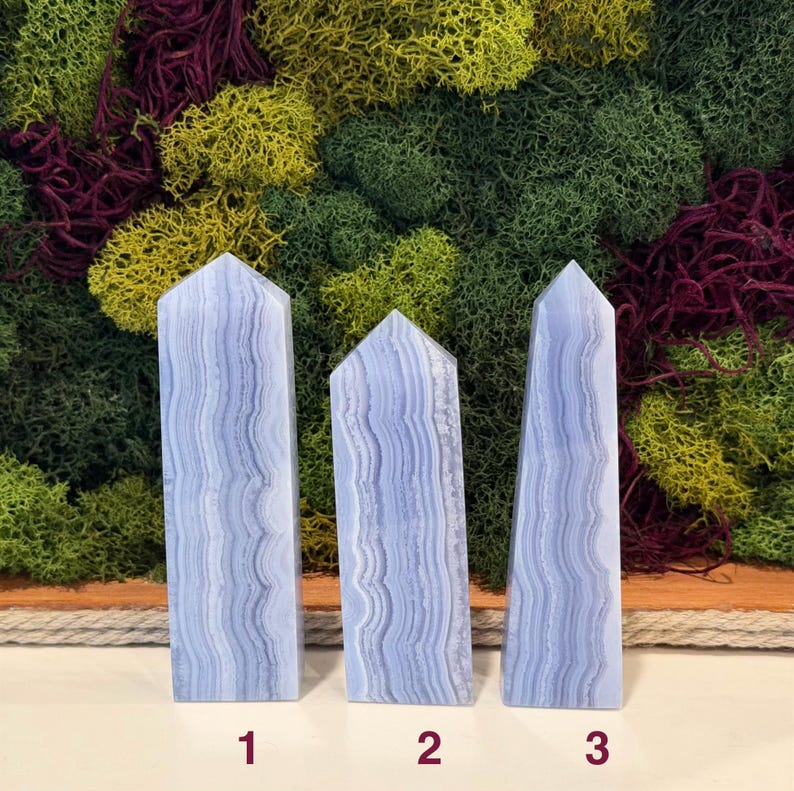 May include: Three blue lace agate obelisks with a layered, banded pattern. The obelisks are numbered 1, 2, and 3. The background features a variety of green, yellow, and red moss.