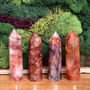 May include: Four red quartz crystal towers with varying patterns and hues. The crystals are numbered 1 through 4. The background features green and burgundy moss.