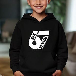 May include: Black hooded sweatshirt with a white graphic design that reads "SIX 6 SEVEN". The sweatshirt has a front pocket and a drawstring hood. The design is centered on the chest.