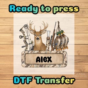 May include: A DTF transfer design featuring a deer head, a compound bow, a rifle, and three ducks hanging by their feet. Below the wildlife imagery is a rectangular camo-patterned nameplate with the name Alex printed in bold black letters.
