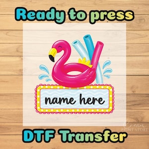 May include: A DTF transfer design featuring a bright pink flamingo pool float with a yellow beak, accompanied by three pool noodles in light blue, teal, and pink. Below the float is a rectangular sign with the text name here in black script.