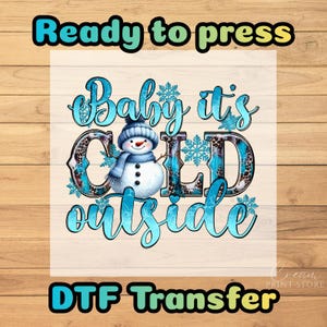 May include: A DTF transfer with the text "Ready to press" and "DTF Transfer". The design features a snowman wearing a blue hat and scarf, with the words "Baby it's cold outside" in a teal script font.