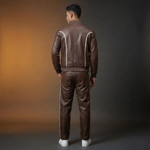 May include: A brown leather track suit with white stripes. The jacket has a bomber style with white accents along the seams. The pants have a matching white stripe down the side. The model is wearing white sneakers.
