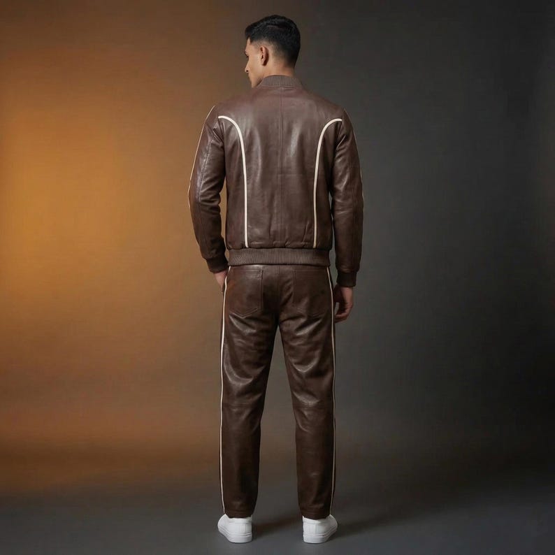 May include: A brown leather track suit with white stripes. The jacket has a bomber style with white accents along the seams. The pants have a matching white stripe down the side. The model is wearing white sneakers.