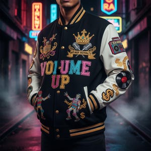 May include: Black varsity jacket with white sleeves, featuring embroidered designs. The jacket has the words "VOLUME UP" in colorful letters, along with a crown and microphone graphic. Other patches include a boombox, dollar signs, and a record.
