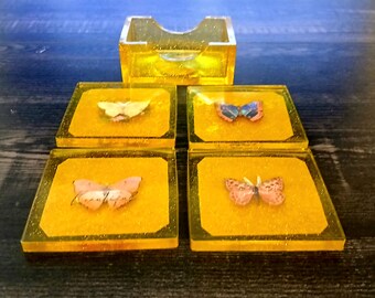 Handgefertigtes Untersetzer Set aus Gießharz. Eingebettete Schmetterlinge, passende Halter, klares Gelb und Glitzerhintergrund