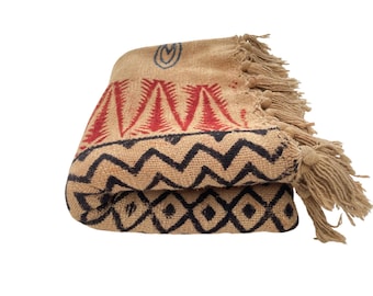 May include: Folded beige throw blanket with red and black geometric patterns. The blanket has a fringe on one end and a blue design in the corner. The blanket is made of a woven material.
