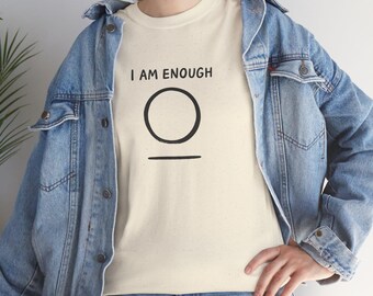 May include: Cream-colored t-shirt with the text "I AM ENOUGH" above a black circle and a horizontal line. The shirt is worn with a light blue denim jacket.