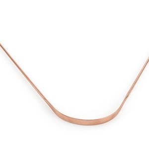 Könnte beinhalten: Ein zungenreiniger in Kupferfarbe mit einer gebogenen, abgeflachten Klinge und zwei Schlaufengriffen. Das Werkzeug ist für die Mundhygiene konzipiert und hat ein schlichtes, minimalistisches Design. Das Metall hat eine polierte Oberfläche.