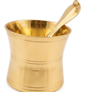 Könnte beinhalten: Ein poliertes, goldfarbenes Mörser- und Stößel-Set aus Messing. Der Mörser hat einen breiten, ausgestellten Rand und einen zylindrischen Körper mit zwei horizontalen, eingravierten Linien in der Mitte. Ein glatter, geschwungener Stößel liegt im Gefäß.