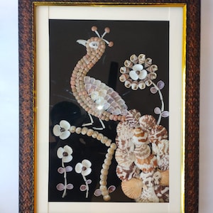 May include: Framed artwork of a peacock made from seashells, set against a black background. The peacock's body and tail are formed from white and tan shells. The frame is dark brown with a textured pattern, and a gold inner border. The artwork is framed.