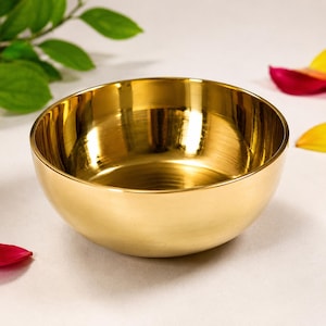 Puede incluir: Un cuenco de metal de color dorado pulido con una superficie lisa y reflectante y una forma redondeada. El cuenco presenta un interior profundo y un acabado metálico consistente, mostrando un brillo luminoso que capta la luz en sus paredes curvas.