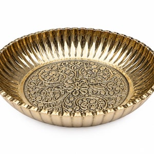 Op de afbeelding: Een ronde, goudkleurige metalen schaal met een gepolijste afwerking. De binnenkant van de bodem is voorzien van een ingewikkeld, in reliëf gemaakt bloemmotief met krullende ranken en bladeren. De zijkanten hebben een verticale, geribbelde rand.