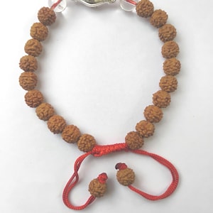 Peut inclure: Bracelet de perles marron texturées, montées sur un cordon rouge. Il comporte un fermoir argenté et des perles rondes transparentes. Le cordon rouge réglable se termine par deux petites perles. Longueur: environ 18 cm.